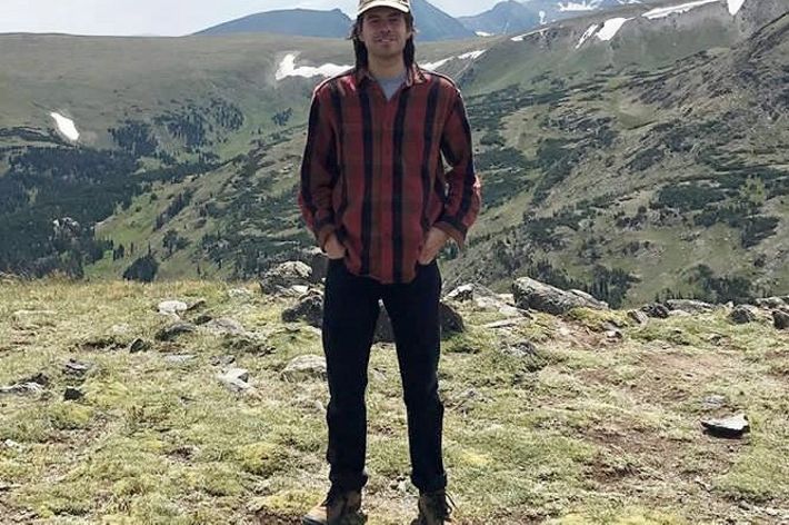 Joe Galarraga stands in a rocky clearing with tall mountains rising behind him.