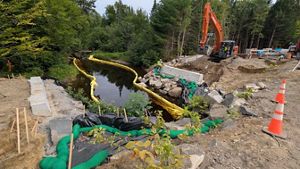 A culvert replacement construction site with an excavator, erosion controls, and workers installing rock and concrete structures along the waterway.
