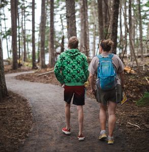 Two people walk along a paved path that winds through a forest.