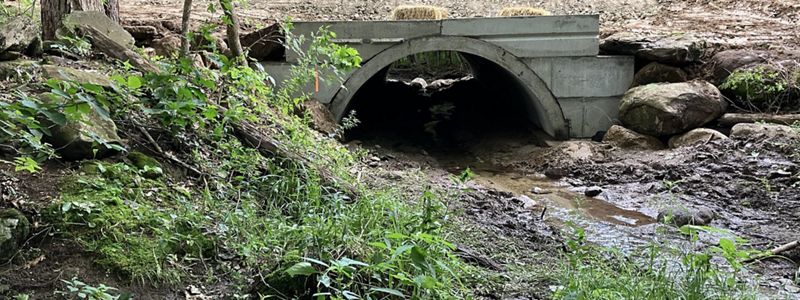 Large concrete structure over a stream in a wooded area.