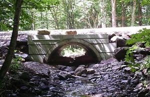 After photo of a stream in a wooded area, flowing freely through a large concrete structure.