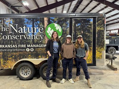 Three women stand in front of a trailer with The Nature Conservancy logo on it.