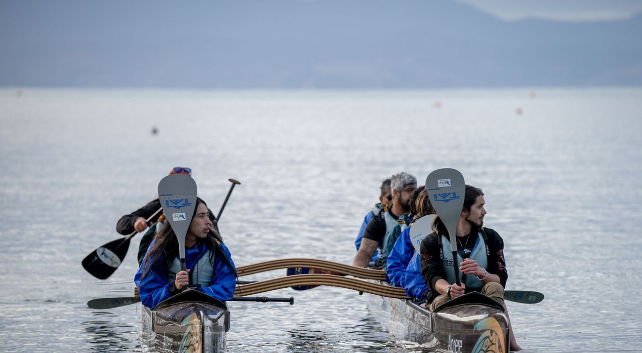 People in a boat holding paddles vertically while looking to their left.