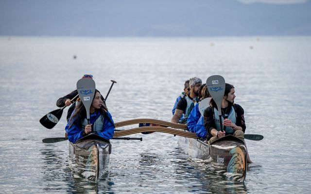 Several people sit in waka (canoes) on flat water.