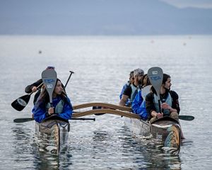 People in a boat holding paddles vertically while looking to their left.