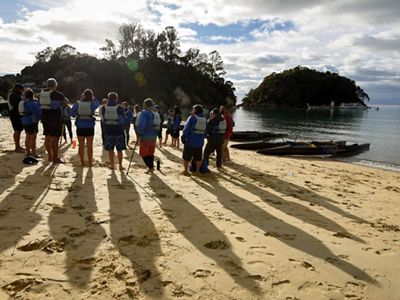 Paddlers stand in a circle on the shote near their boat holding a meeting.