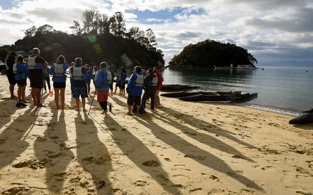 Several people stand on a beach as the sun rises over them.