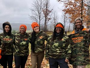 Five participants in the hunting weekend stand outdoors smiling at the camera. Each are wearing either a camouflaged t-shirt or sweatshirt that includes "HOC" printed.