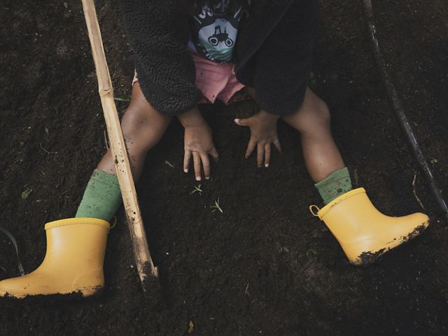 toddler sits on farm in yellow rainboots.