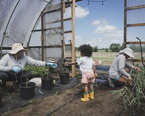 Three women sit and farm in a high tunnel.