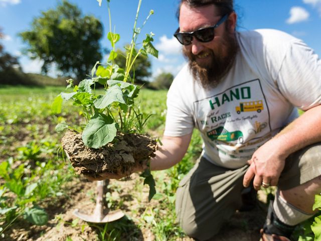 A smiling, bearded man holding a plant.