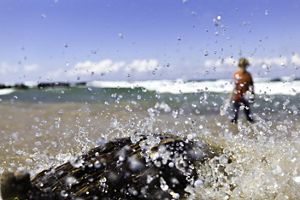 A young boy enjoys the shoreline of Lake Superior on a windy day. He is out of focus in the background while crashing water droplets along the shore are in focus.