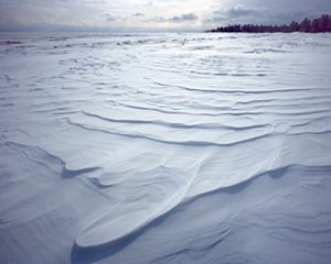 Snow drifts along the shore of a lake.