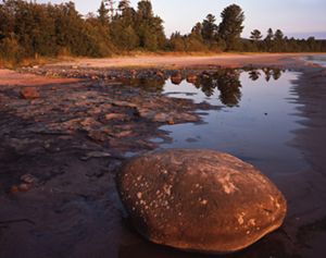 Large and small rocks are deposited on the sandy shore of a lake.