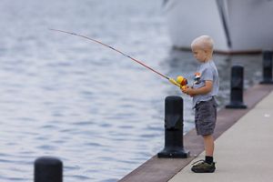 A young boy stands at the edge of a pier with a fishing rod in hand.