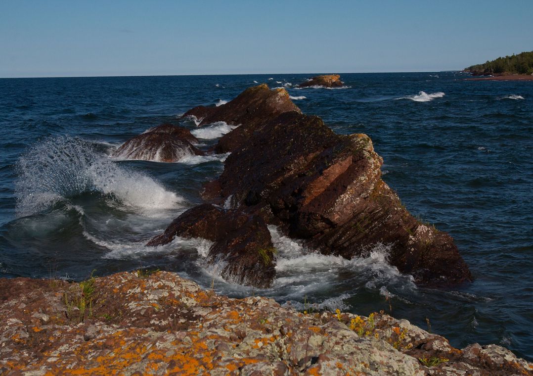 Rocks jutting out of Lake Superior on the Mary Macdonald Preserve shoreline under a blue sky. The preserve is located in the Keweenaw Peninsula in Michigan's Upper Peninsula.