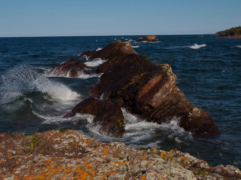 Rocks jutting out of Lake Superior on the Mary Macdonald Preserve shoreline under a blue sky. The preserve is located in the Keweenaw Peninsula in Michigan's Upper Peninsula.