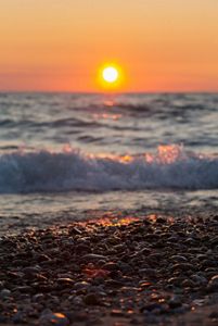 Close up wave hitting a pebbled beach at sunset.
