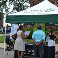 Two people stand at a TNC outdoor event tent and speak to a TNC staff member.