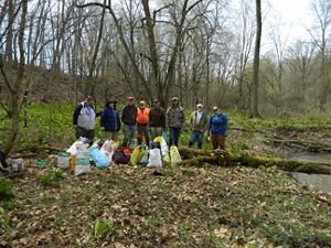 A group of 8 people stand by the water of the Ives Road Fen in Michigan. They are surrounded by bags and other supplies.