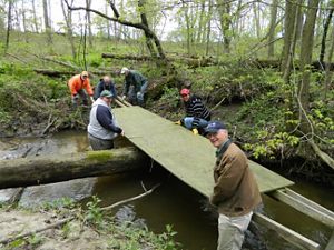 A group of six people secure a bridge over water at Ives Road Fen Preserve in Michigan. 