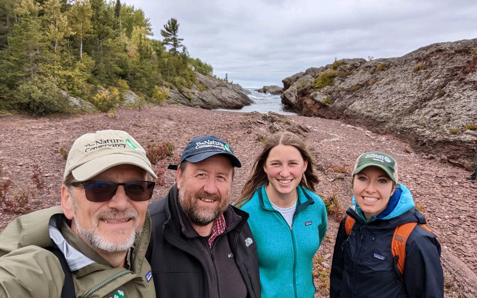 Four people smiling with rocks and water in the distance. 