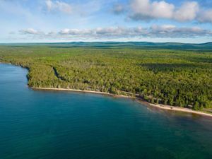 Aerial view of the still water of Lake Superior along the wooded Little Betsy Shoreline in the Keweenaw on a clear day.