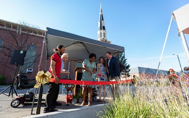 A group of five people gather around a red ribbon in front of Sacred Heart Church at the ribbon-cutting ceremony.