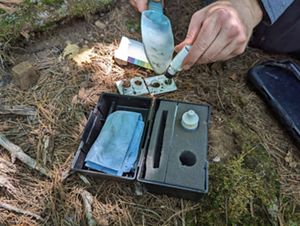 A person uses a soil pH kit on a forest floor. 
