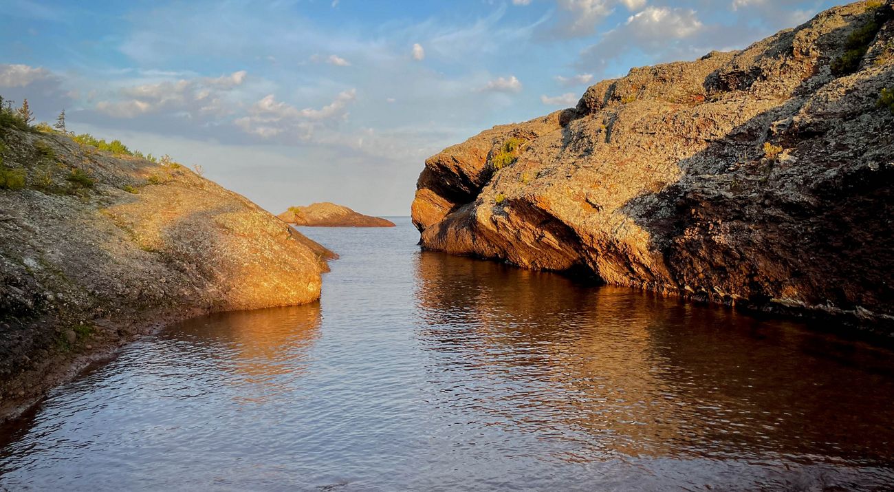 Water between two large rock formations, covered in lichen and other plants, along the shore of Lake Superior in the Keweenaw Peninsula of Michigan.