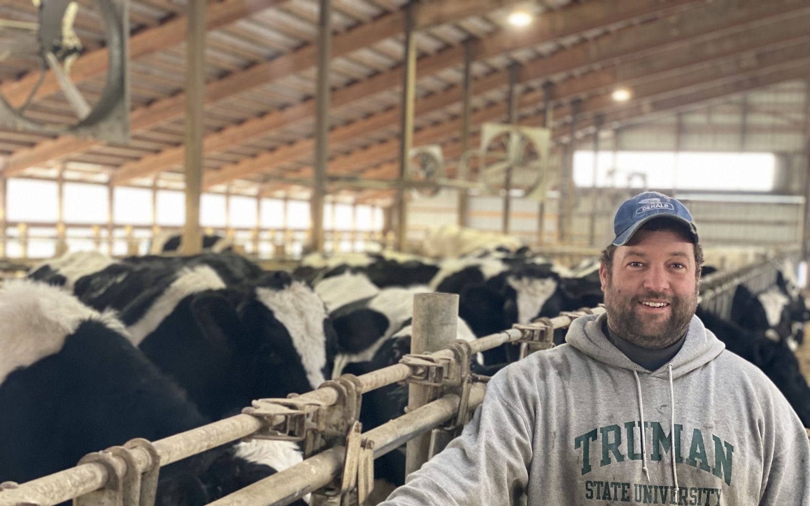 A representative from Pohl Dairy smiles at the camera. They are surrounded by cattle.