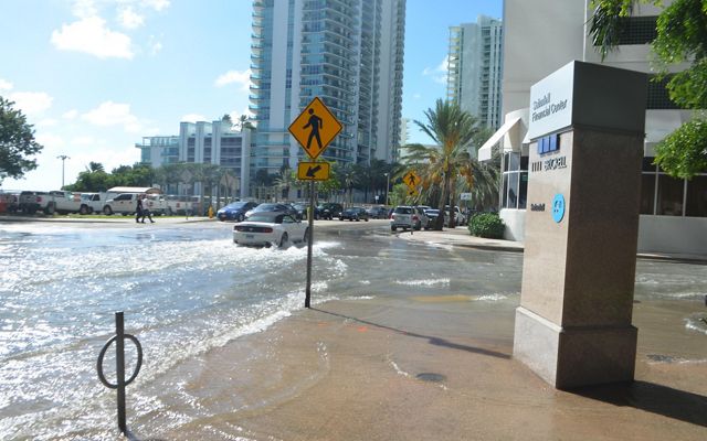 Urban streets with traffic are flooded as water runs over sidewalks.