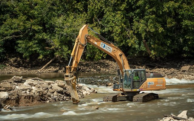 A large yellow machine with a long front arm conducts restoration work in the Mississippi River.