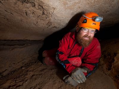 A man in a dark cave wearing a helmet with a light on it.
