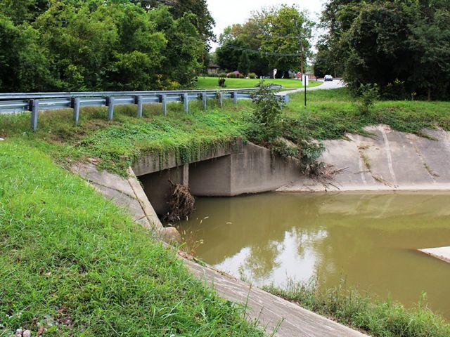 A bridge crosses over a brown creek lined with a cement wall.