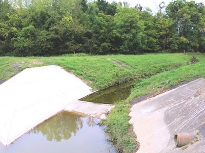 Concrete ramps frame a creek flowing through a grassy landscape.