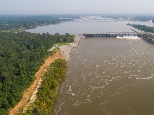 A brown river flows interrupted by a dam that crosses the entire expanse.