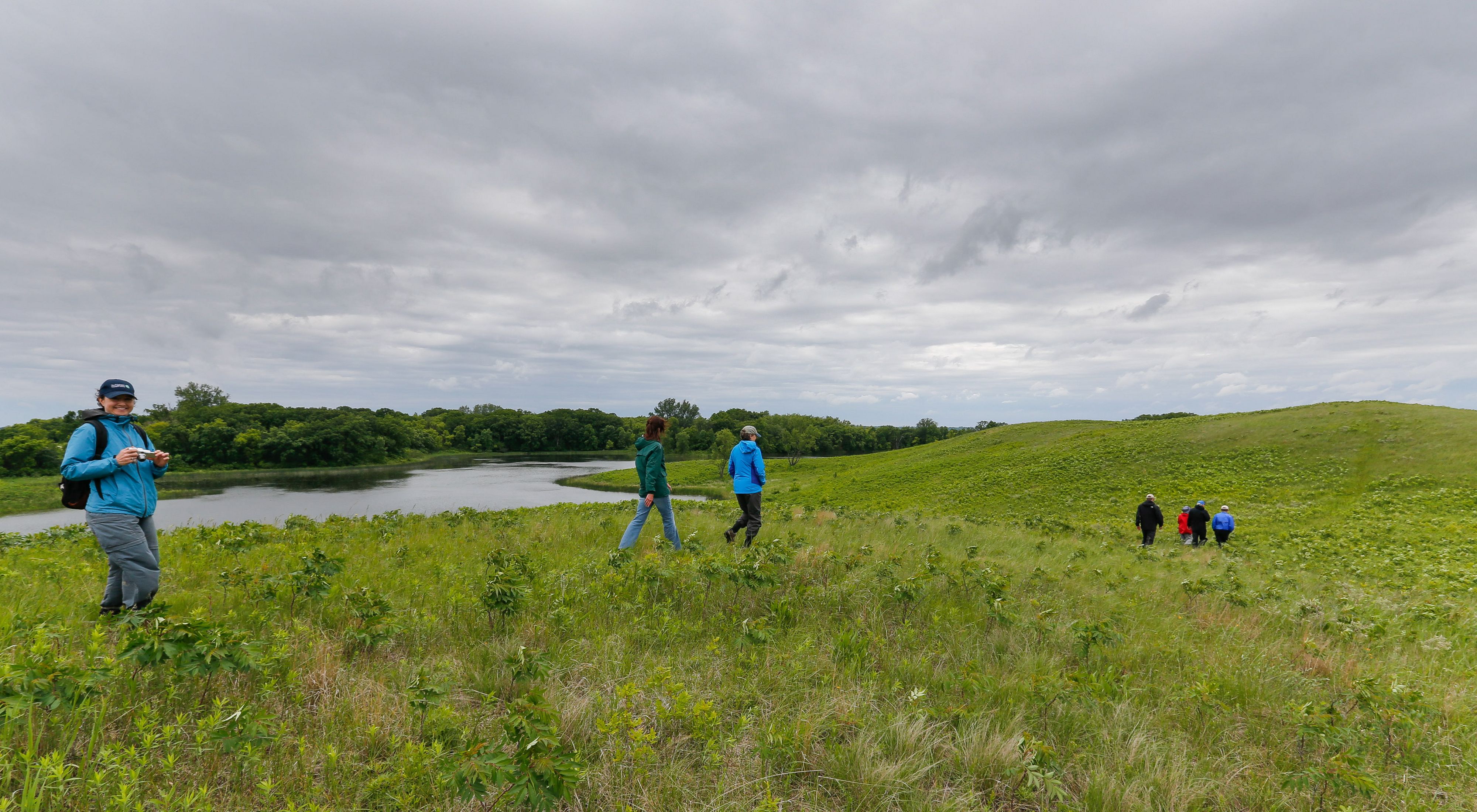 People hiking on a green, rolling prairie alongside a pond at  Northern Tallgrass Prairie National Wildlife Refuge.