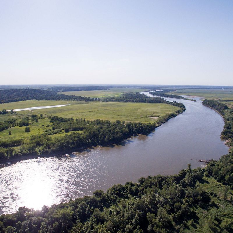 An aerial view of a larger river running through agriculture fields and forested buffers.