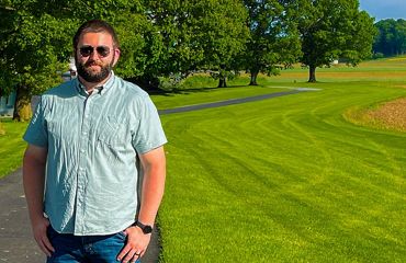 A photo of Mitchel Zimmerman in front of a field.