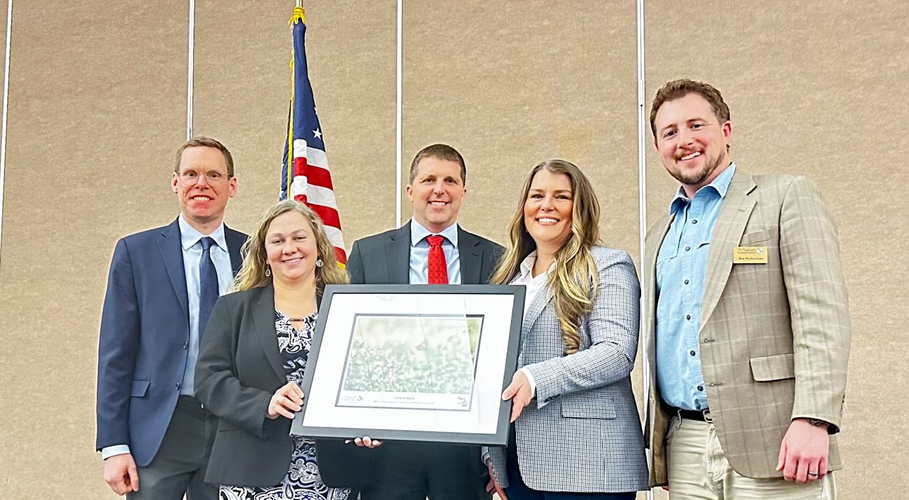 Five people stand on a stage holding an award photo.