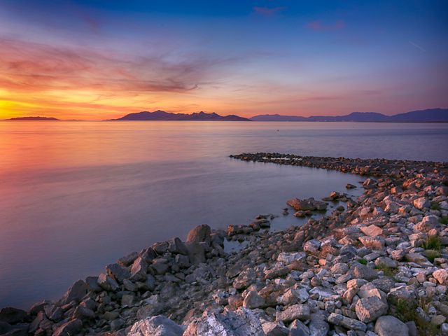 Looking across the Great Salt Lake at sunset; a rock jetty extends out into the lake, and the water is various shades of orange and blue.
