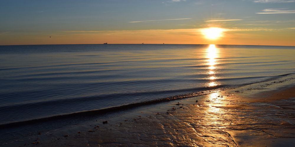 A sun sets over a body of water, creating a yellow and orange reflection.
