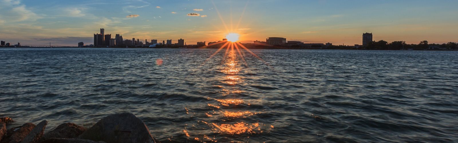 View from the water of sun setting behind the Detroit skyline.
