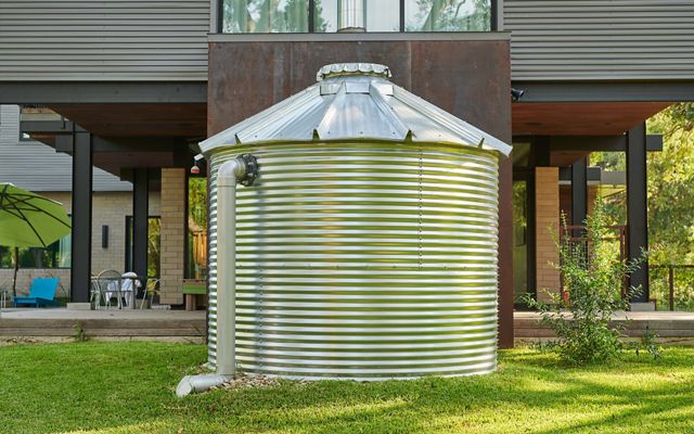 A large steel rain cistern sits outside a home.