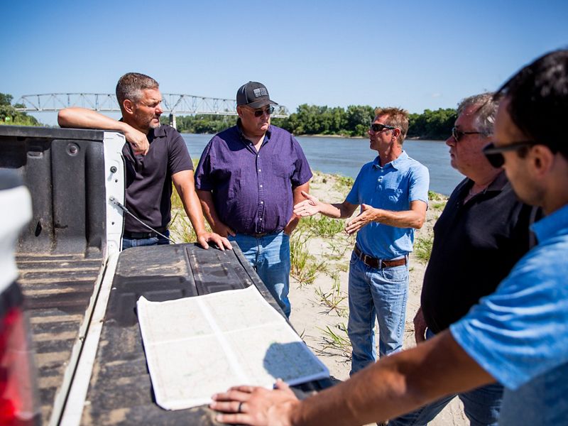 Group of men looking at map on the back of a pickup truck.