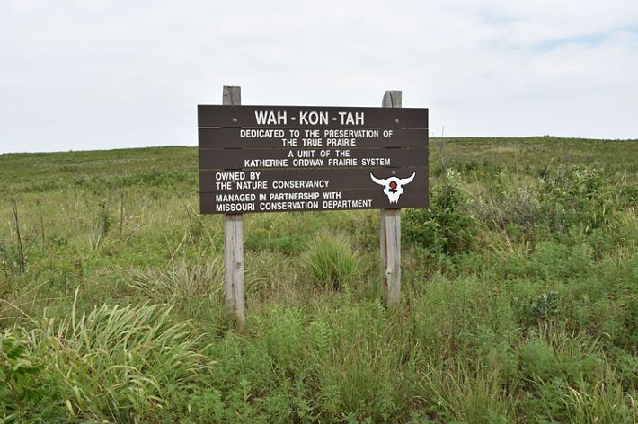 A wooden sign with preserve name 'Wah-Kon-Tah' on it sits in an open prairie field.