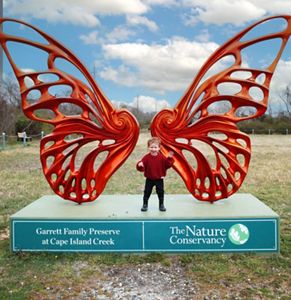 A child standing in front of a large, orange butterfly statue.