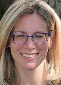Headshot of Monica Anzaldi. She has shoulder-length blonde hair and wears blue glasses.