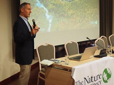 Josh Royte stands and holds a microphone with a presentation projected on a screen behind him.